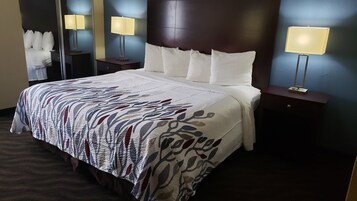 Una habitación de hotel con una cama grande, cabecera, dos mesitas de noche con lámparas y un espejo.
