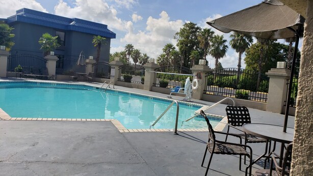 A swimming pool with a blue-tiled edge, surrounded by lounge chairs and a covered seating area. - Red Roof Inn Port Allen West LSU Stadium (Port Allen)