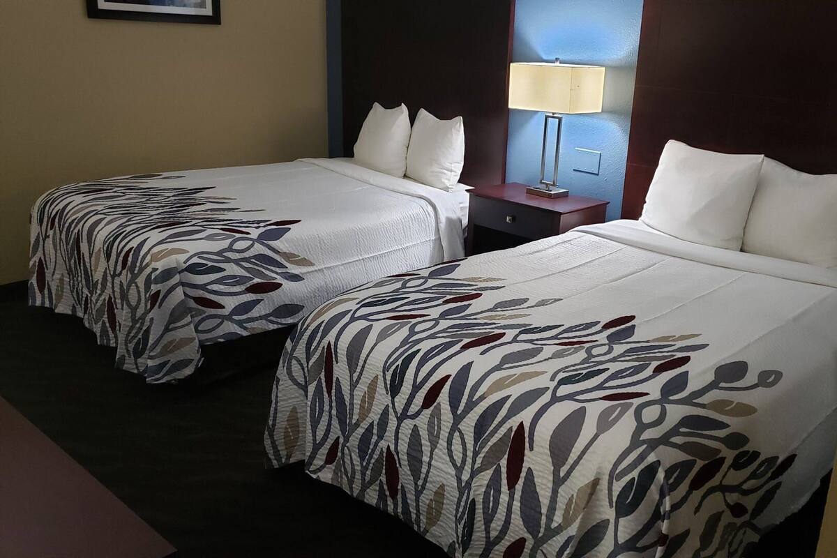 Two double beds with leaf-patterned bedding, a nightstand with a lamp, and a dark headboard.