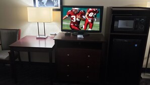 A hotel room with a TV, a desk, a chair, a lamp, a microwave, and a small refrigerator. - Red Roof Inn Port Allen West LSU Stadium (Port Allen)