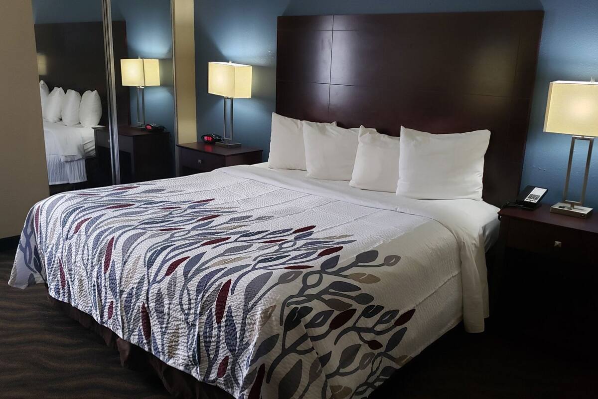 A hotel room with a large bed, two bedside tables with lamps, a mirror, and a nightstand with a phone.