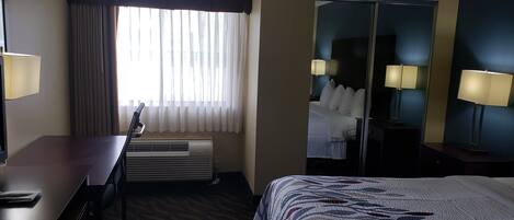 Ein Hotelzimmer mit Bett, Schreibtisch, Stuhl, Spiegel und einem Fenster mit Vorhängen.