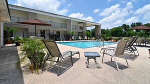A poolside area with lounge chairs, umbrellas, and a building with balconies. - Motel 6 Luling, LA (Luling)
