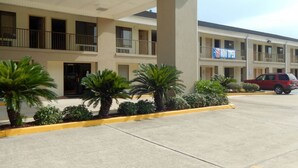 A motel with a two-story structure, a balcony on the second floor, and a parking lot with a red car. - Motel 6 Luling, LA (Luling)