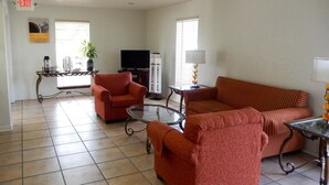 A living room with a red sofa, a glass coffee table, a television, and a coffee station. - Motel 6 Luling, LA (Luling)