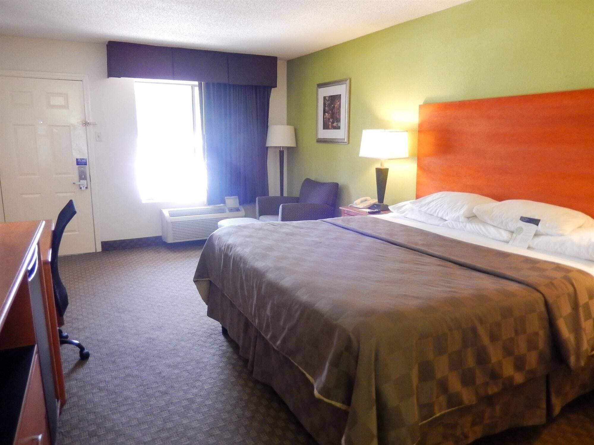 A hotel room with a large bed, a desk, a chair, a lamp, and a window with curtains.