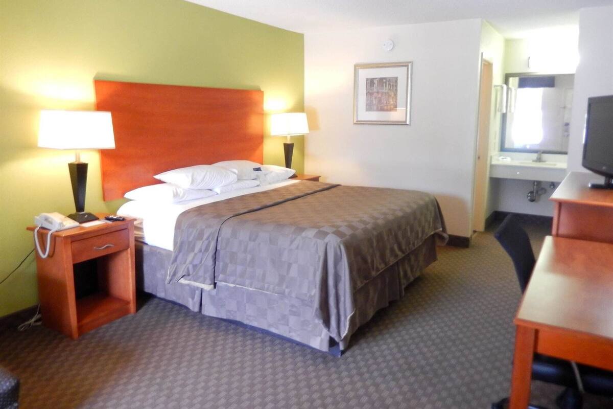 A hotel room with a bed, bedside lamps, a telephone, a desk, and a television.