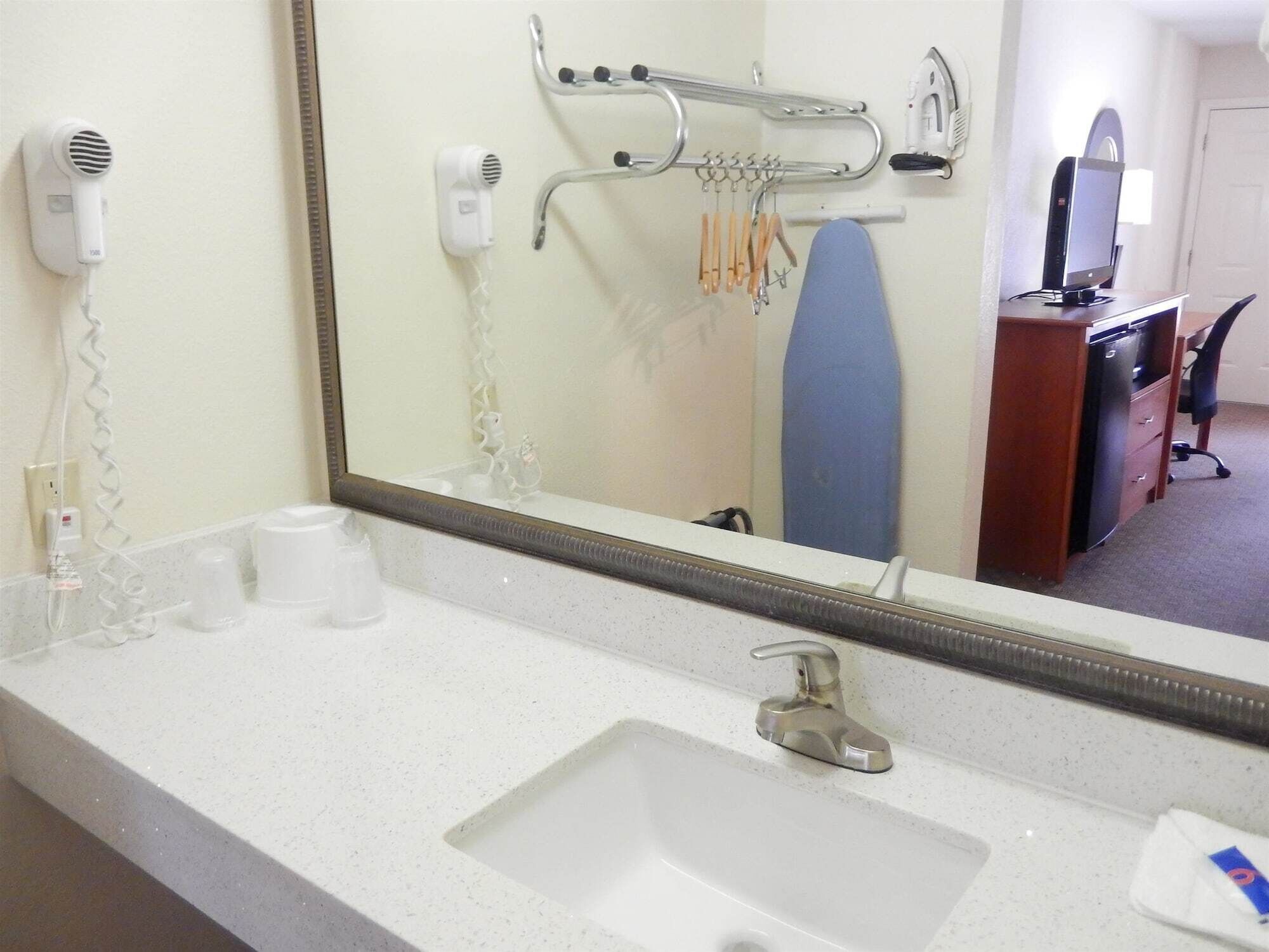 A hotel bathroom with a sink, mirror, hairdryer, and ironing board.