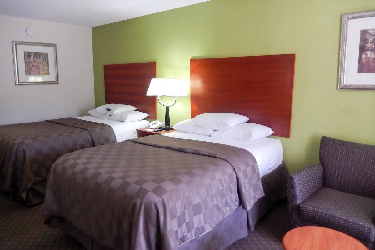 A hotel room with two beds, a nightstand, a lamp, a chair, and a framed picture on the wall.