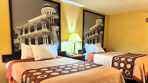 A hotel room with two beds, a nightstand, a lamp, and a large framed picture of a building on the wall.