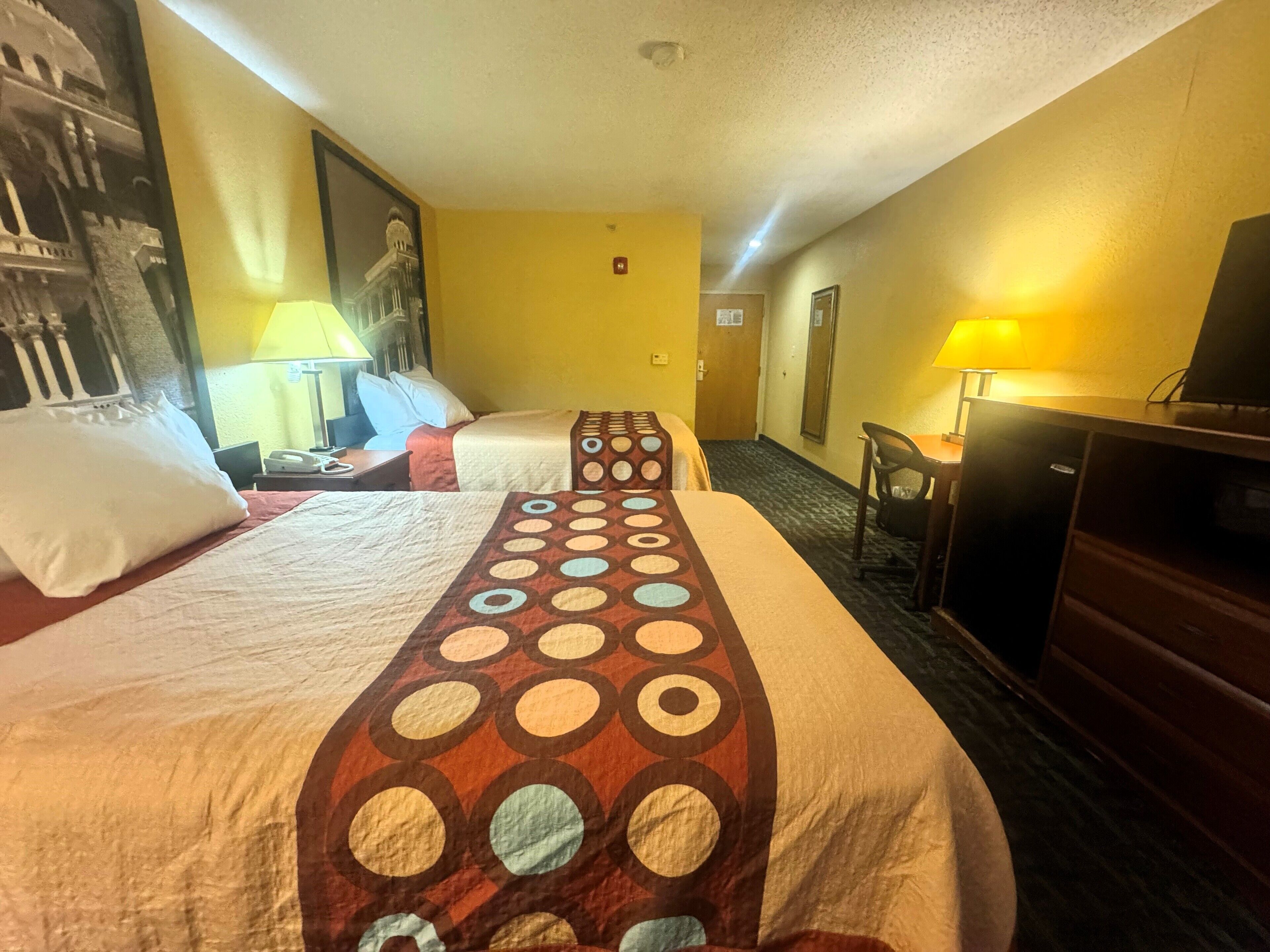 Een hotelkamer met twee bedden, een bureau, een stoel, een televisie en een lamp.