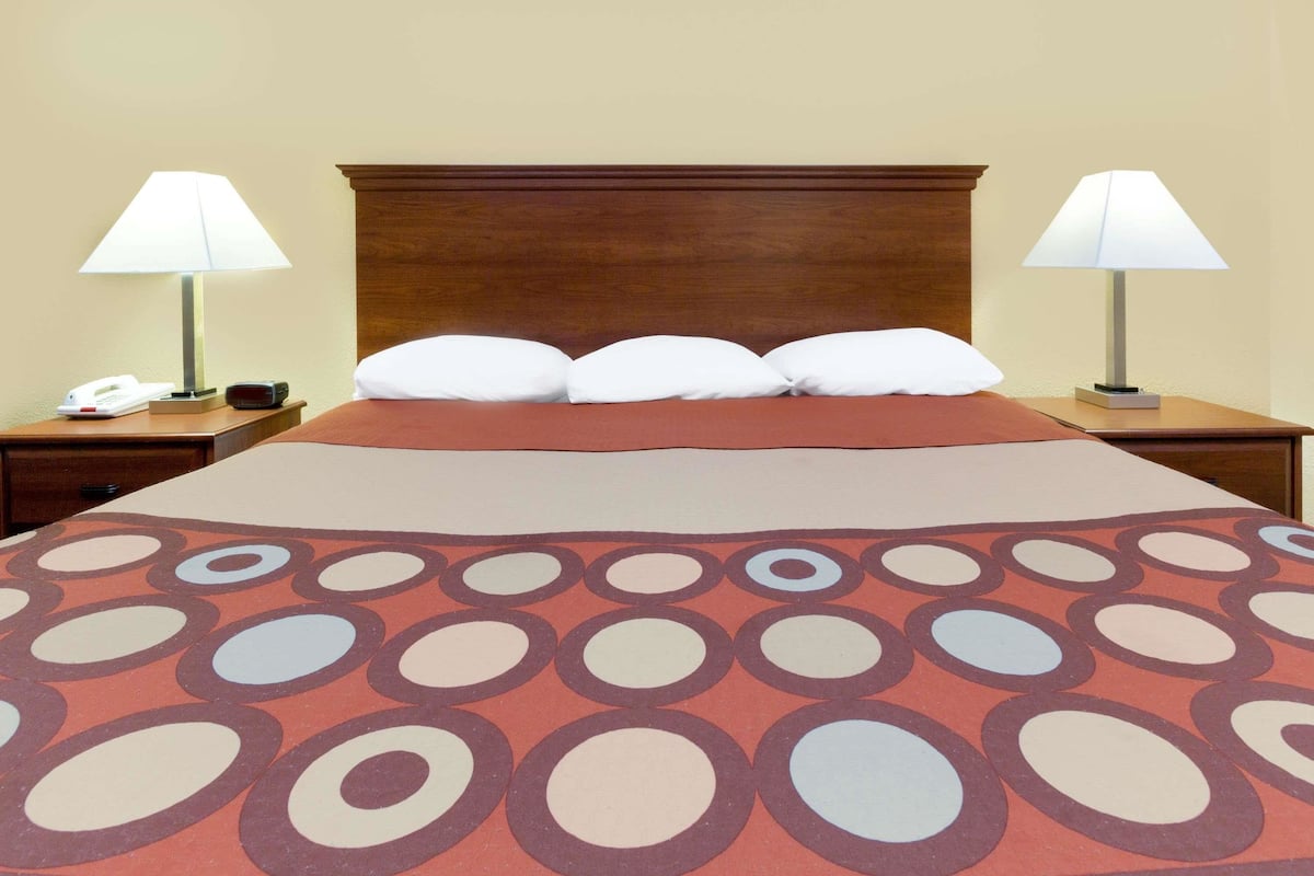 Quarto de hotel com uma cama grande, duas mesas de cabeceira, um painel de cabeceira de madeira e um edredom estampado.