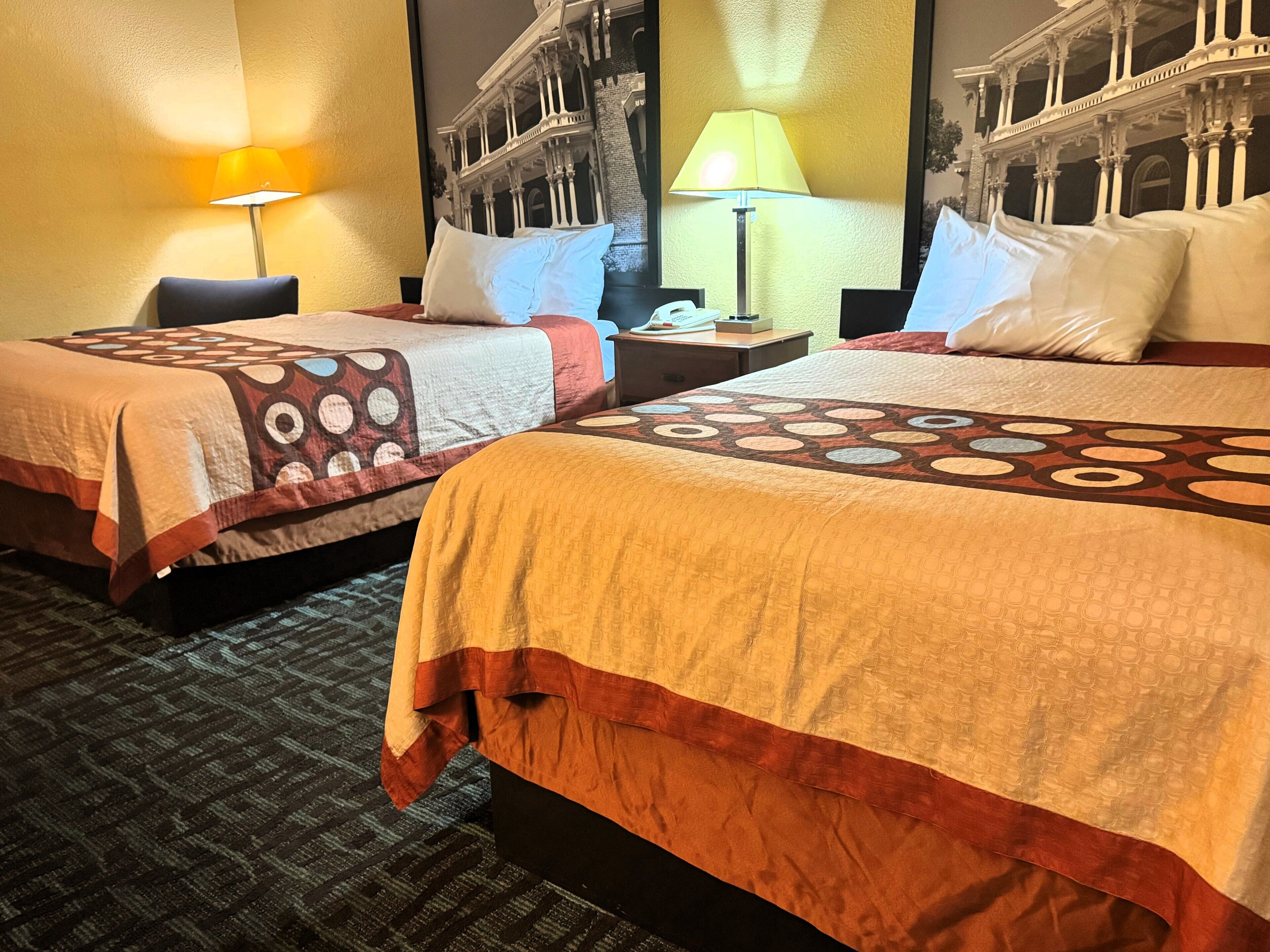 Habitación de hotel con dos camas, cada una con cubrecamas estampados, una mesita de noche con lámpara y un espejo grande que refleja la decoración del cuarto.