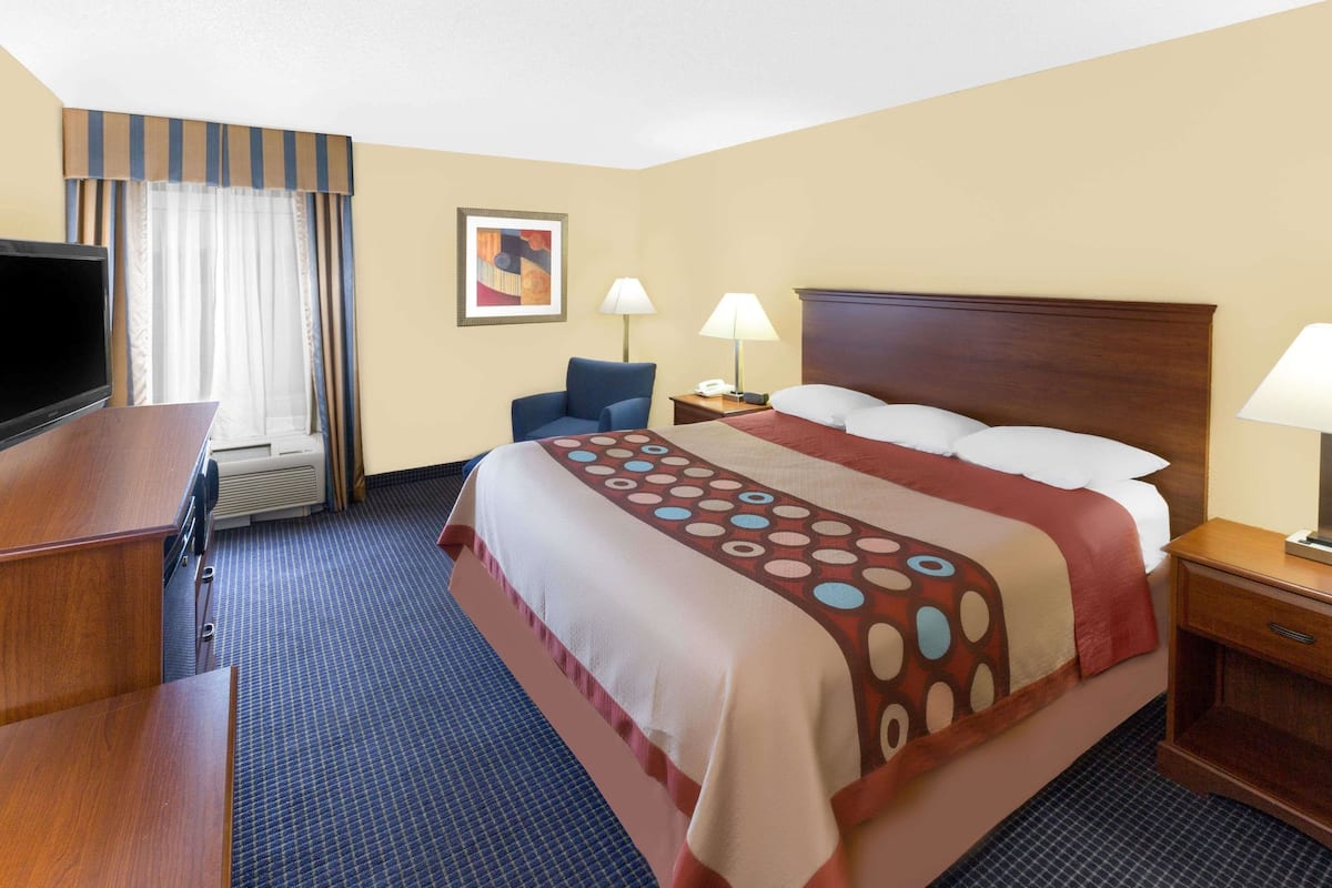 Quarto de hotel com cama, escrivaninha, cadeira, duas luminárias e televisão.