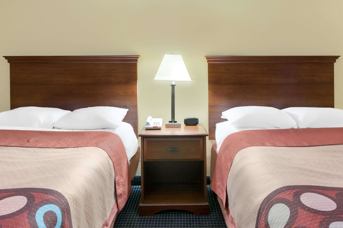 Quarto de hotel com duas camas, uma mesa de cabeceira com abajur, telefone e rádio.