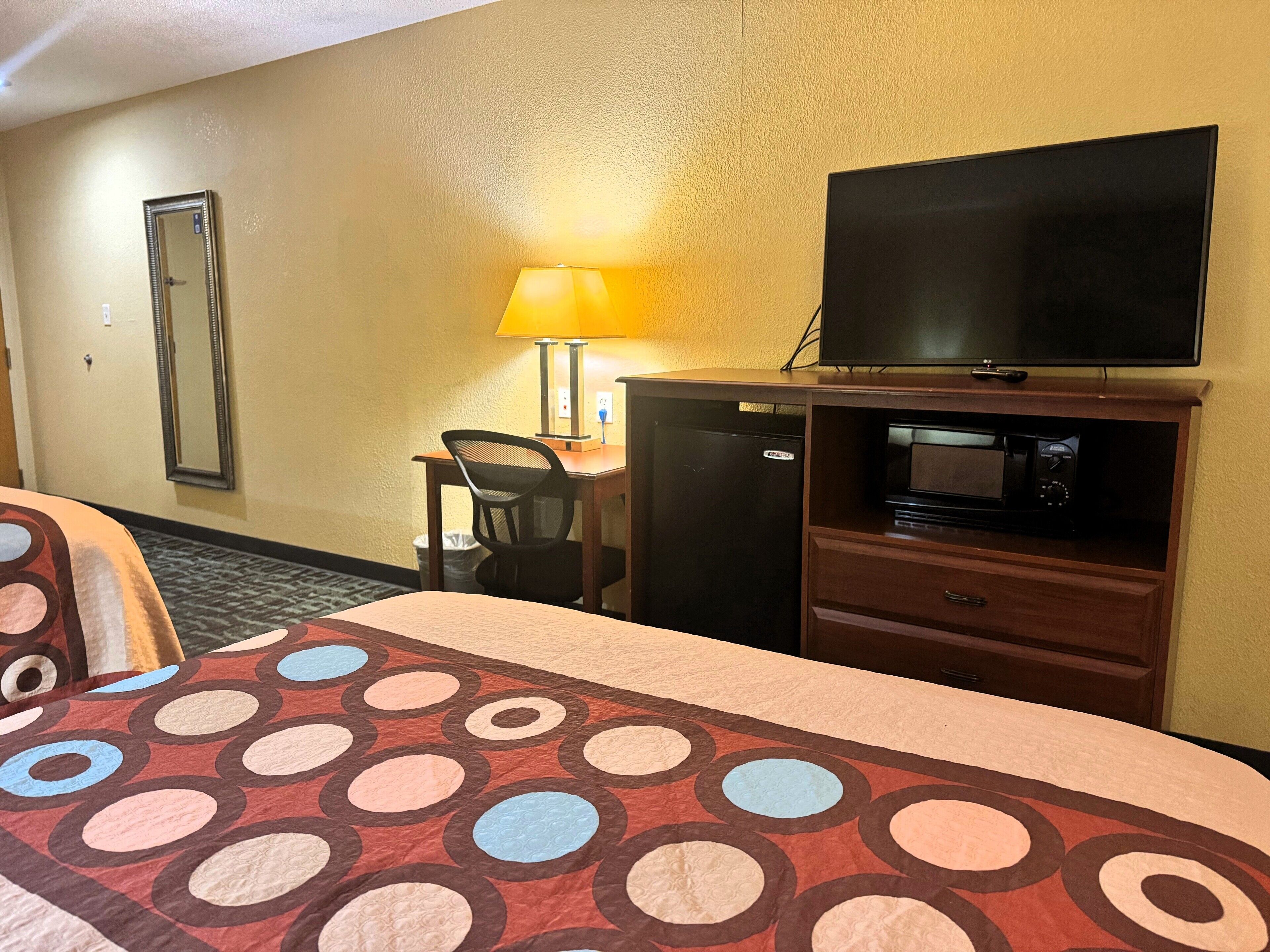 Habitación de hotel con cama, escritorio, televisor, microondas y cesto de basura.