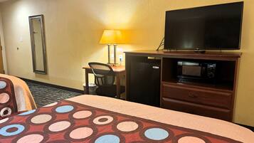 Habitación de hotel con cama, escritorio, televisor, microondas y cesto de basura.