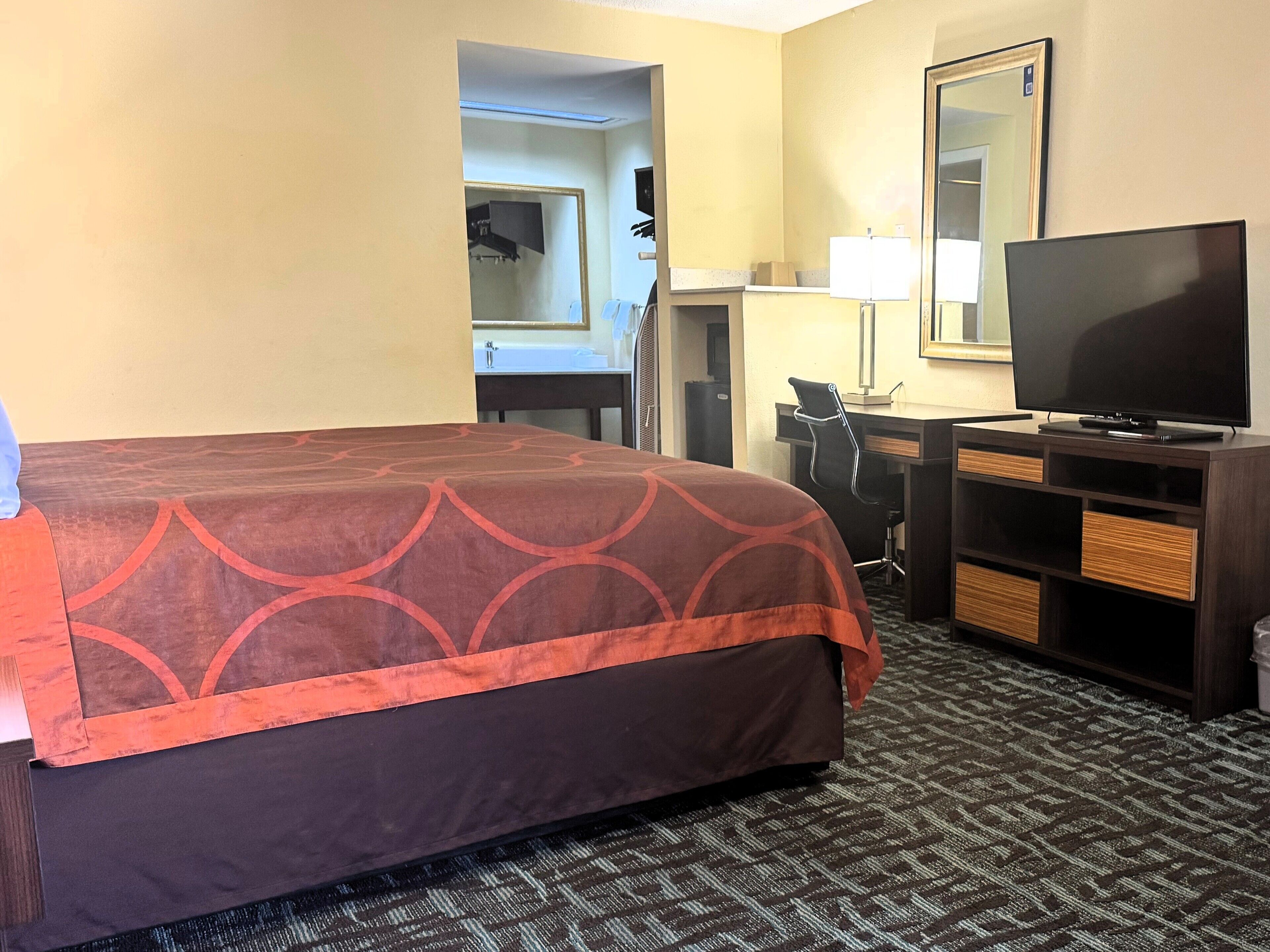 A hotel room with a large bed, a desk with a chair, a television, and a mirror.