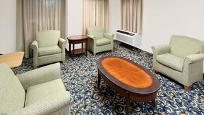 A hotel room with a patterned carpet, two armchairs, a round table, and a large window with curtains.