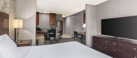 Una habitación de hotel con una cama grande, televisión, escritorio y kitchenette.