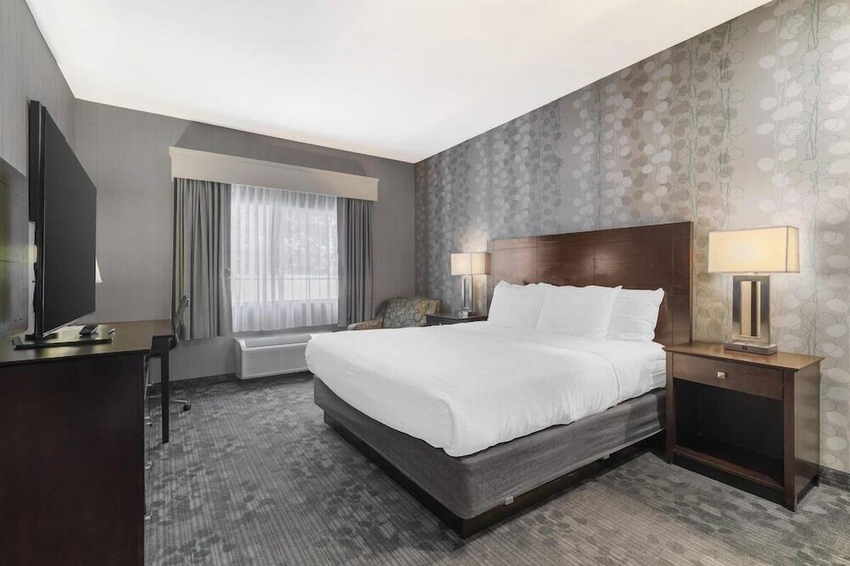 A hotel room with a large bed, a desk with a TV, a chair, and a window with curtains.