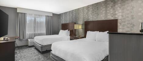Een hotelkamer met twee bedden, een bureau, een televisie en een raam met gordijnen.