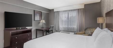 A hotel room with a large bed, a flat-screen TV, a desk with a lamp, and a chair.