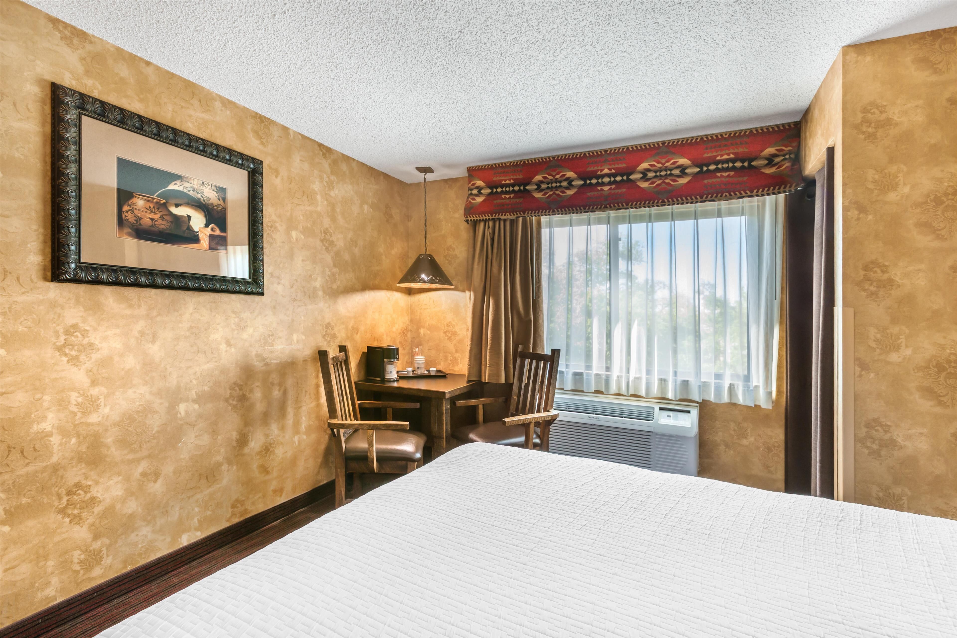 A hotel room with a large bed, a desk with a lamp, a chair, and a window with curtains.