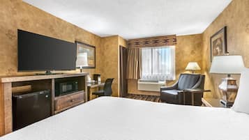 Habitación de hotel con una cama grande, un televisor de pantalla plana, un escritorio con silla, un microondas y un equipo de aire acondicionado.