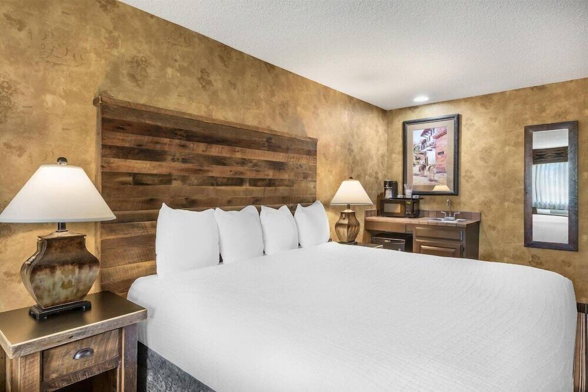 Une chambre d’hôtel avec un grand lit, deux tables de chevet avec des lampes, une tête de lit en bois, un bureau avec une chaise, un miroir et un tableau au mur.