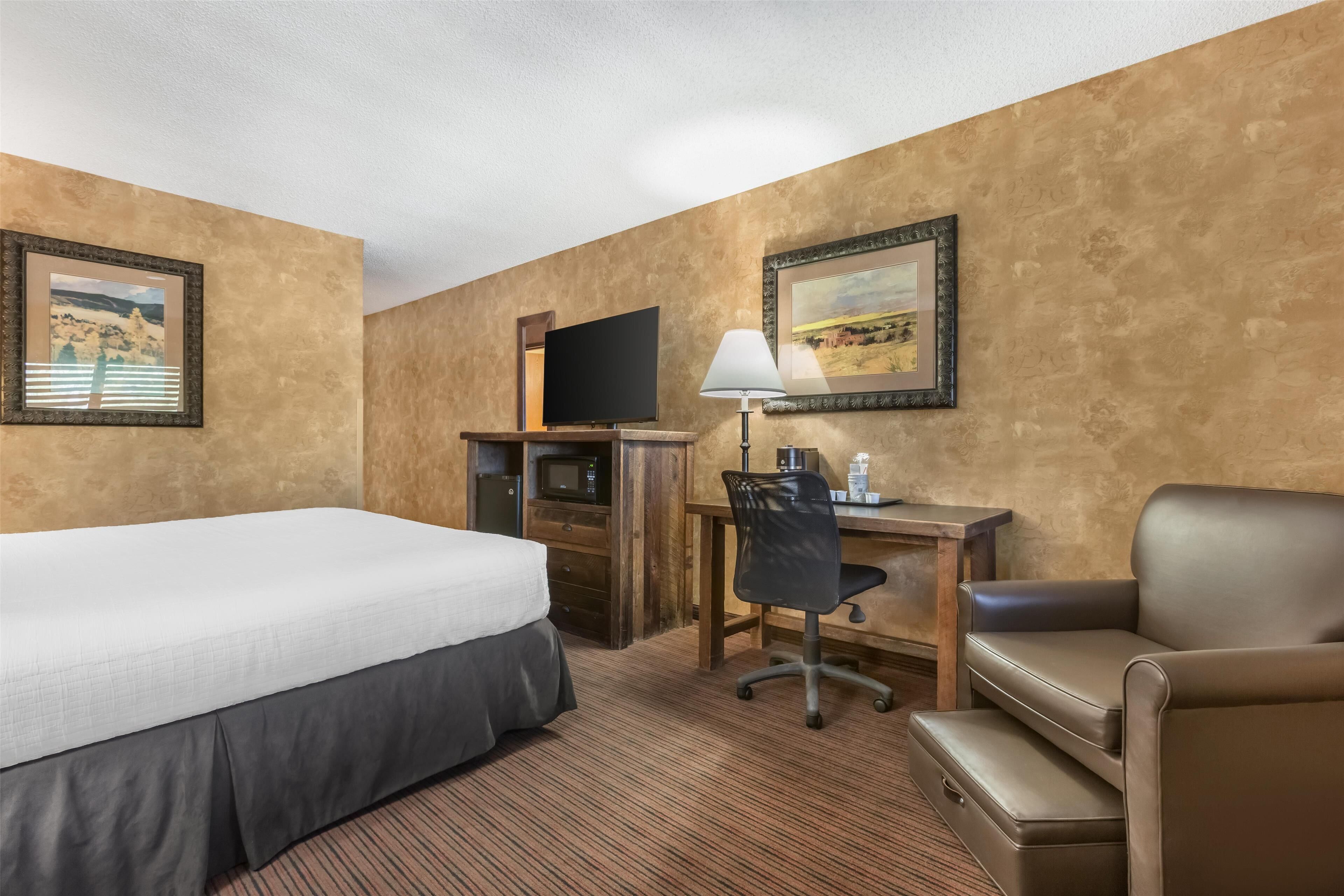 Ett hotellrum med en säng, ett skrivbord, en stol, en tv och en lampa.
