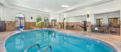 An indoor swimming pool with clear water, surrounded by stone walls and a tiled floor.