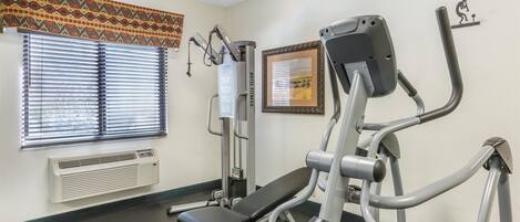 Et fitnessrum med en motionscykel, et styrkeapparat og en bænk.