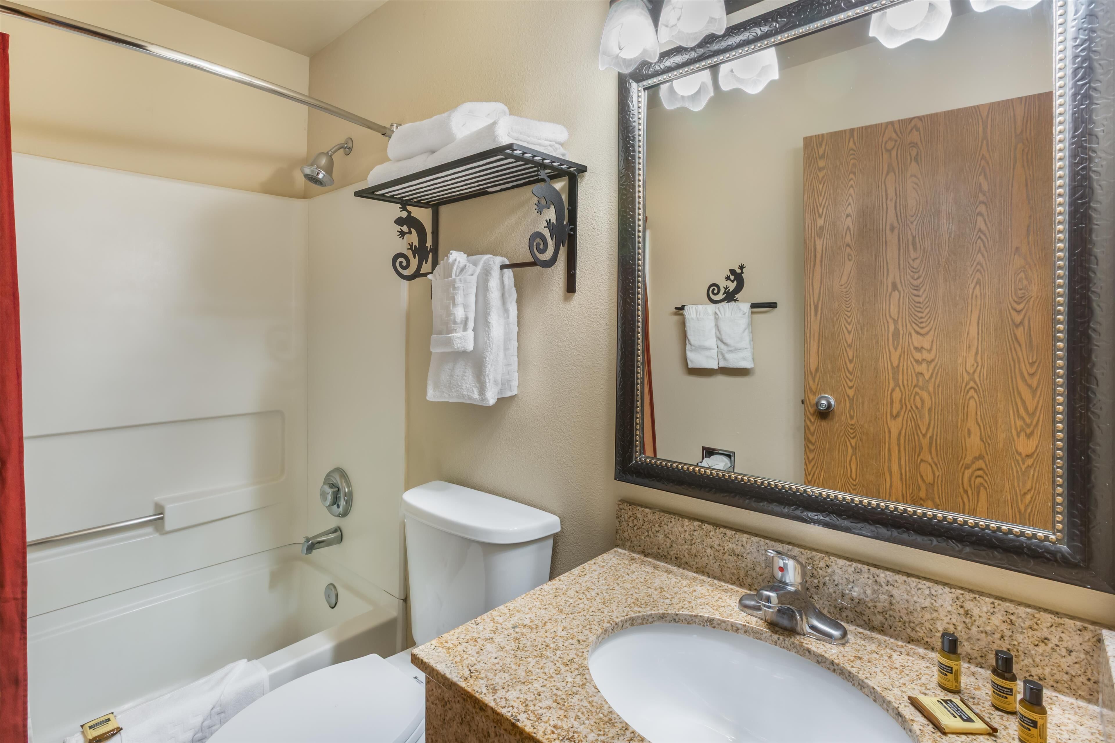 A bathroom with a white bathtub, a sink with a granite countertop, a mirror with a wooden frame, and a towel rack with folded towels.