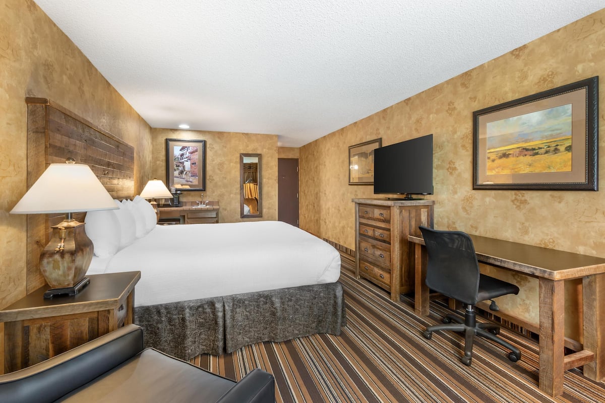 A hotel room with a large bed, a desk with a chair, a television, and a dresser.