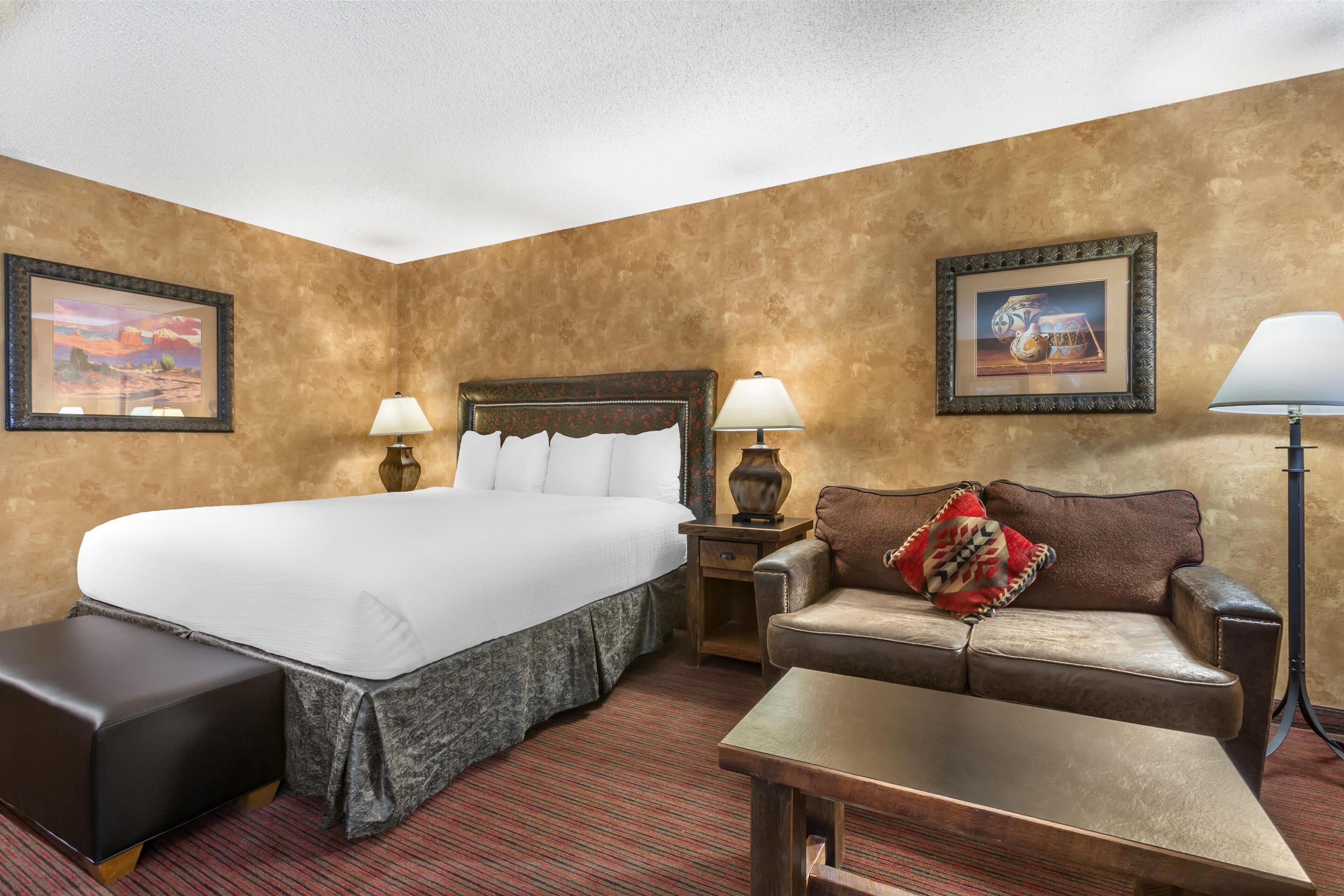 A hotel room with a large bed, a sofa, a small table, and two lamps.