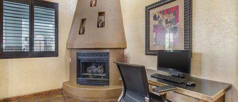 A room with a fireplace, a desk with a computer, and a window with blinds.