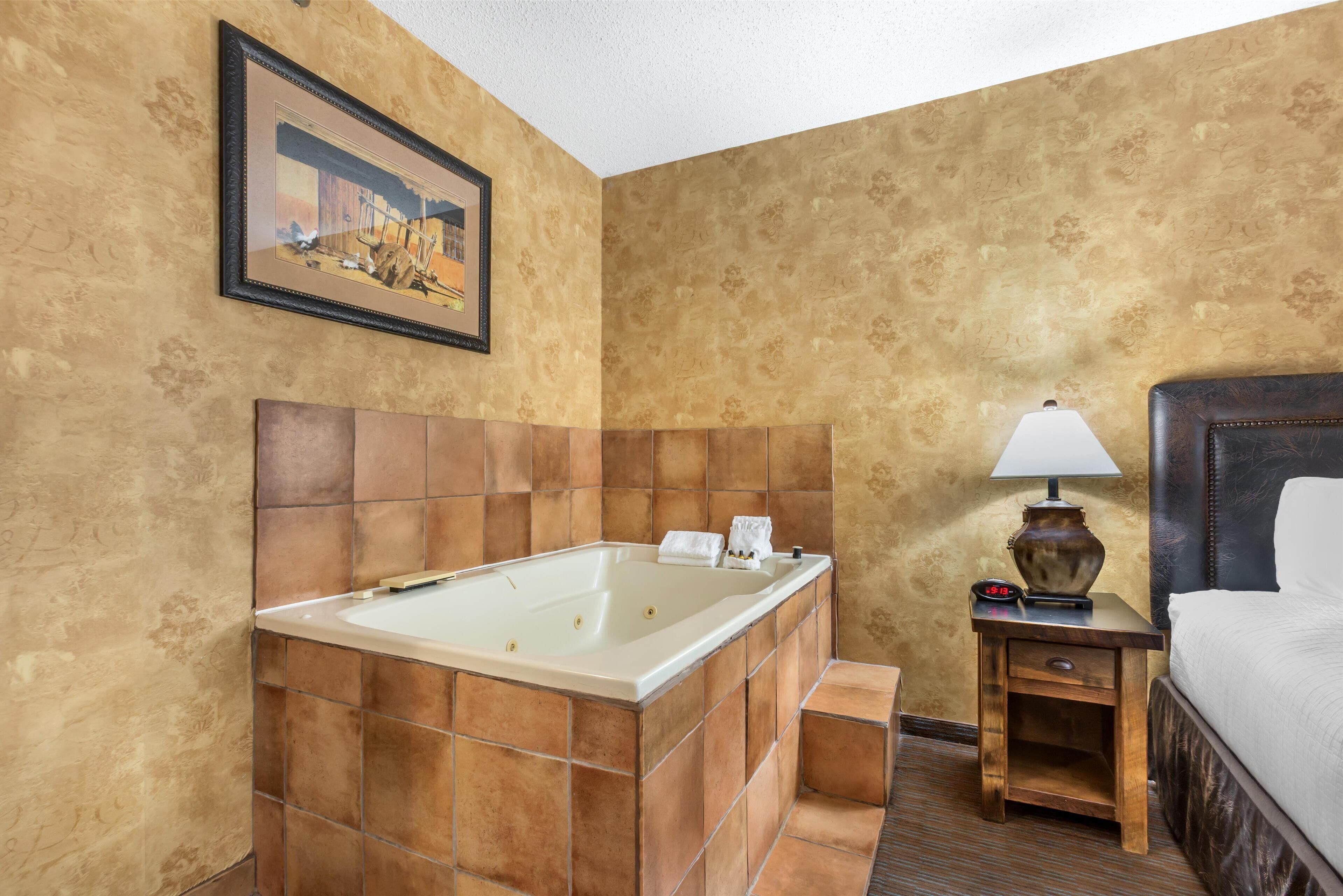 Ein Hotelzimmer mit einer großen Badewanne, einem Nachttisch mit Lampe und einem gerahmten Bild an der Wand.