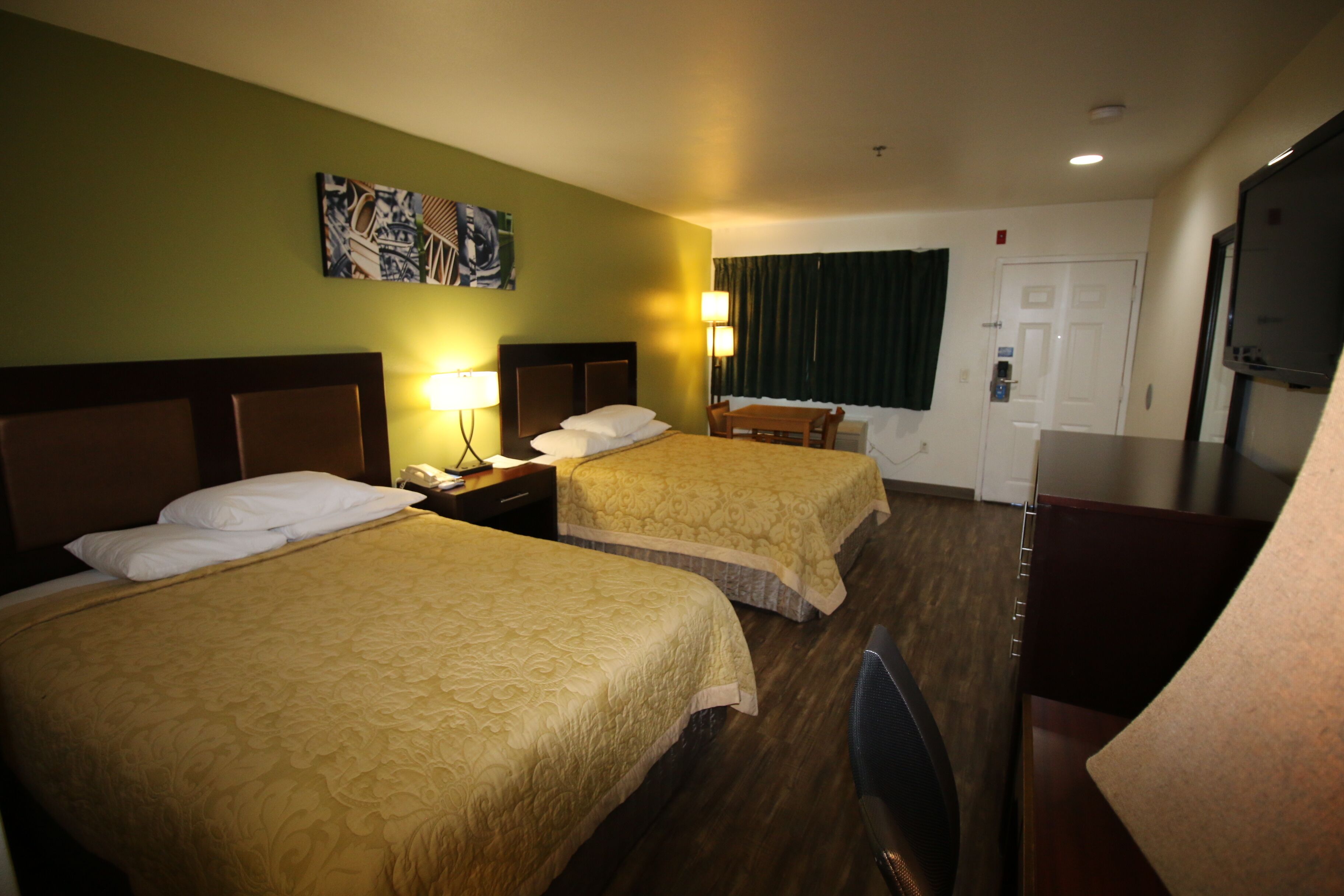 A hotel room with two beds, a desk, a chair, a television, and a painting on the wall.