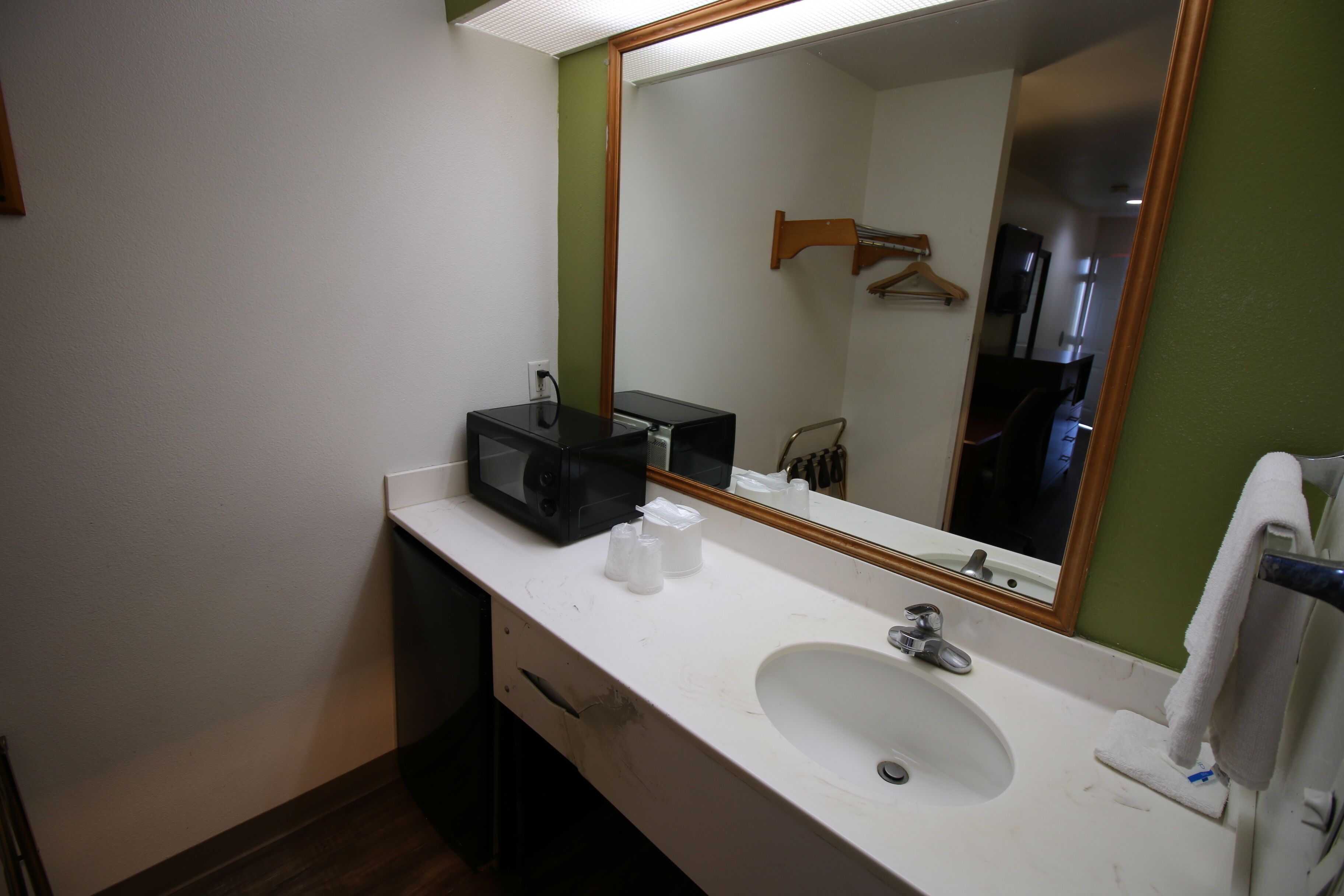 A bathroom with a white sink, a mirror, and a black microwave on the counter.