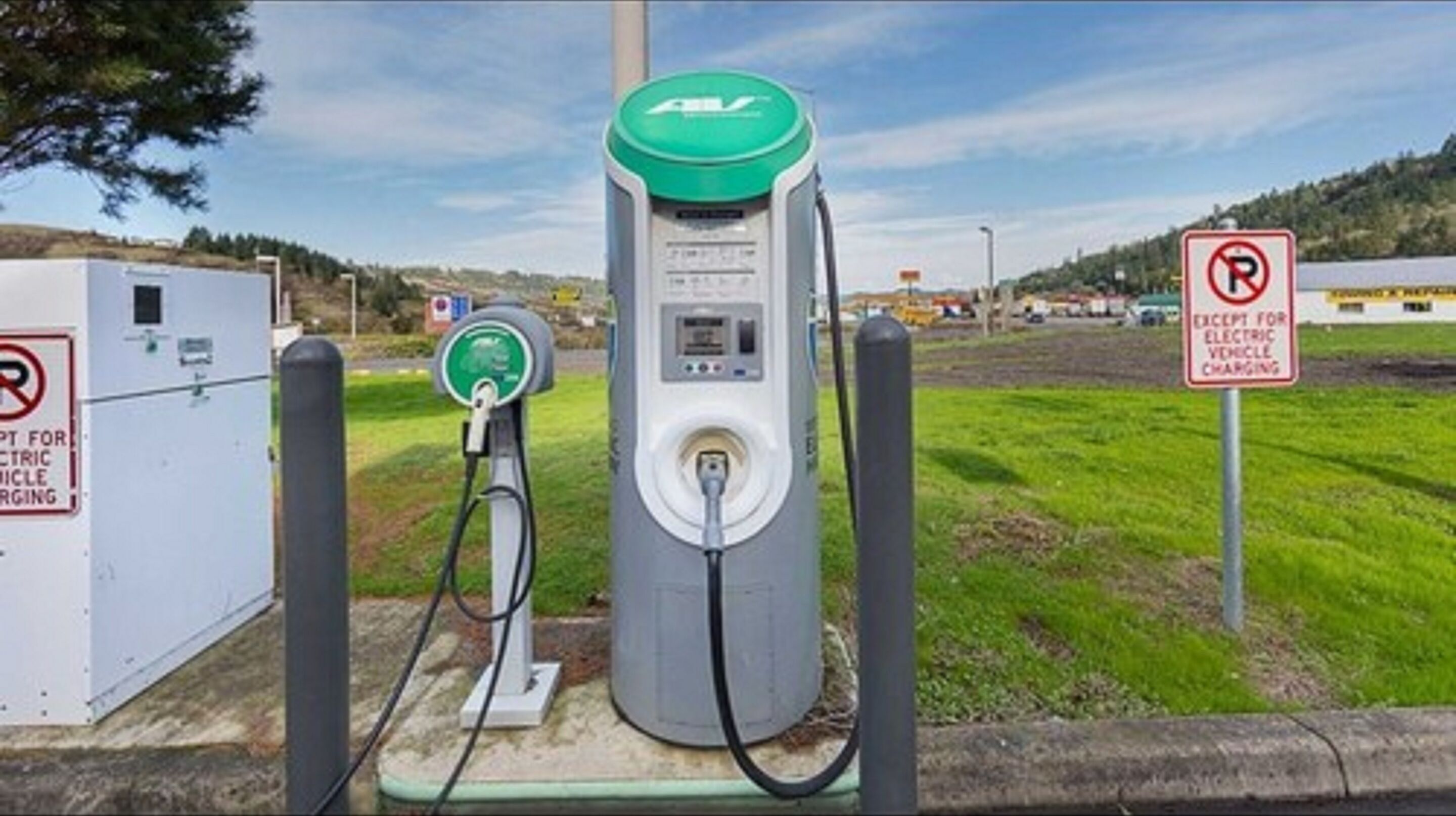 A public electric vehicle charging station with a green top, a digital display, and a charging cable connected to a vehicle.