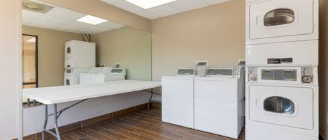 A laundry room with a large table, multiple washing machines, and a mirror on the wall.