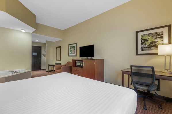 Habitación de hotel con una cama grande, un escritorio con computadora, televisor, silla, lámpara de escritorio y un cuadro en la pared.