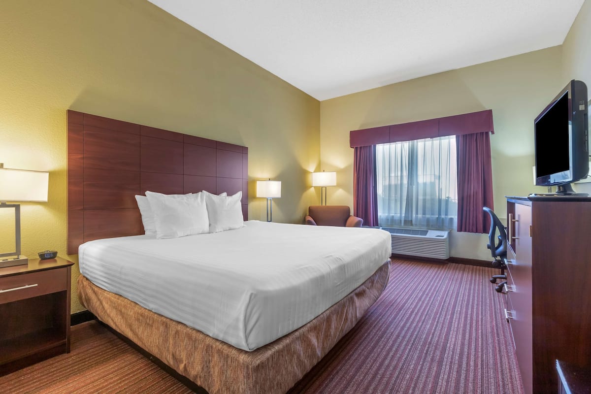 A hotel room with a large bed, two bedside lamps, a television, and a desk with a chair.
