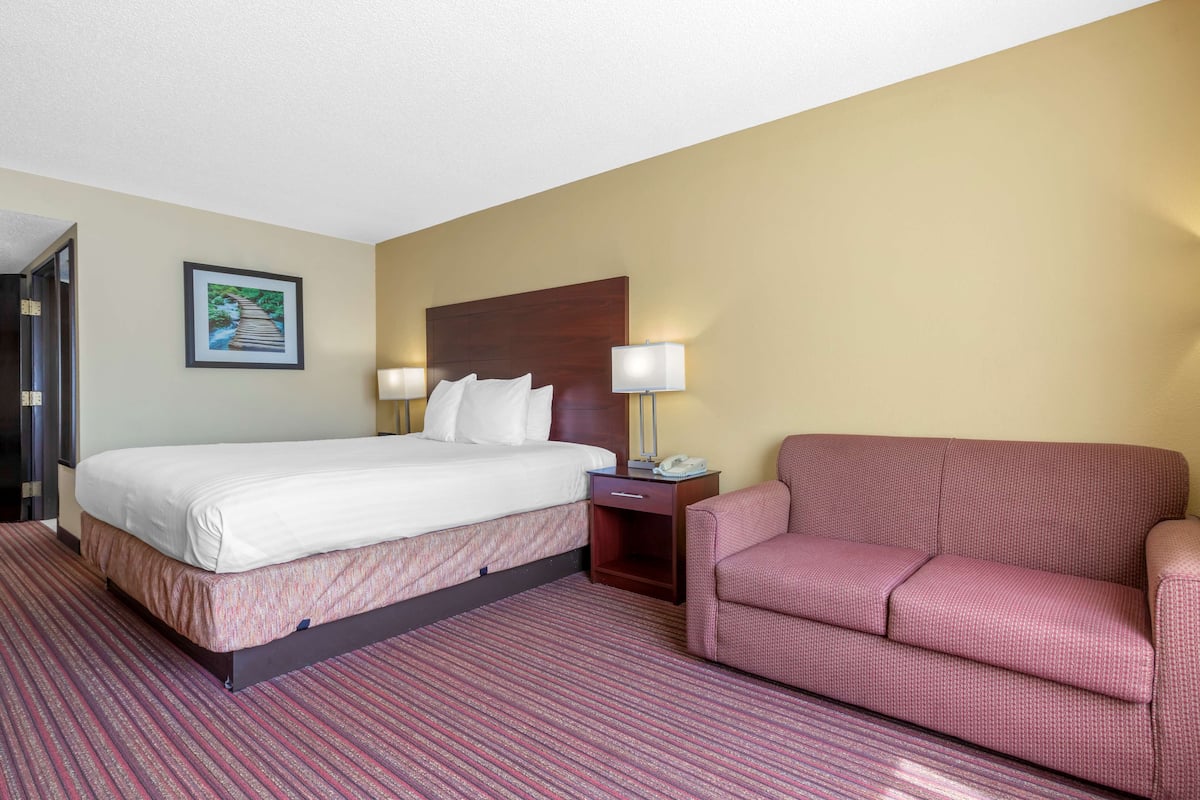A hotel room with a bed, two bedside lamps, a nightstand, a chair, and a framed picture on the wall.