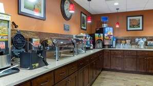 Un comptoir pour le petit-déjeuner équipé d’appareils à gaufres, de machines à café et d’une horloge murale.