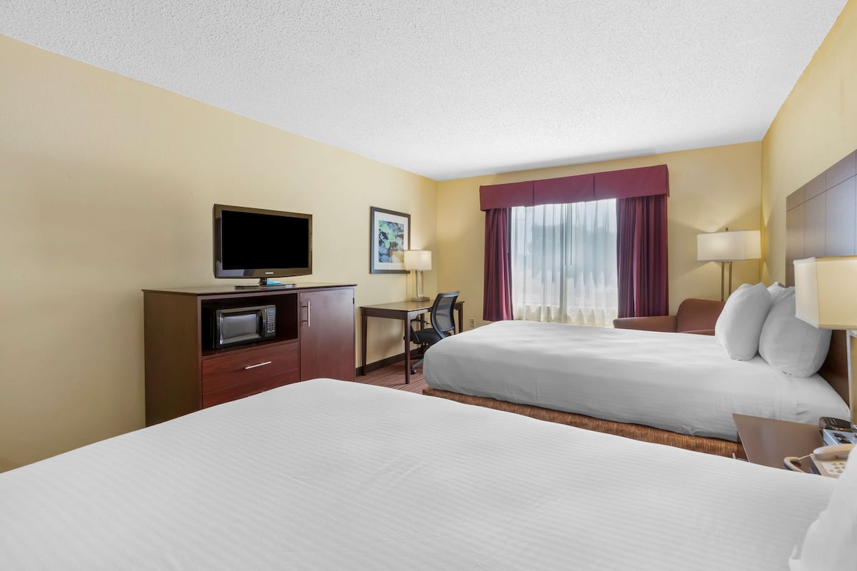 A hotel room with two beds, a desk with a computer, a television, and a window with curtains.