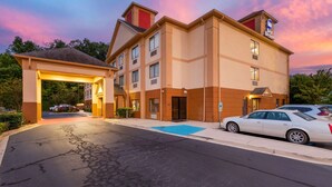 Un hôtel à plusieurs étages, doté d’une entrée imposante, d’un espace de stationnement et d’une voiture garée devant.