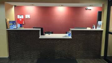 A reception desk with a red wall, a black mat, and a white counter.