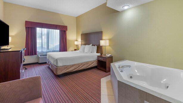 Une chambre d’hôtel comprenant un lit, un bureau, une chaise, une grande fenêtre avec des rideaux, une salle de bain avec une baignoire et un téléviseur à écran plat.